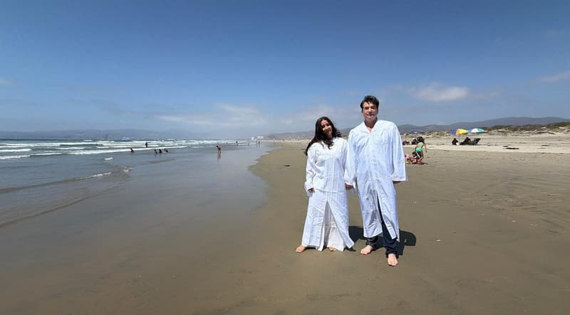 Dos personas con túnicas blancas de pie en una playa.