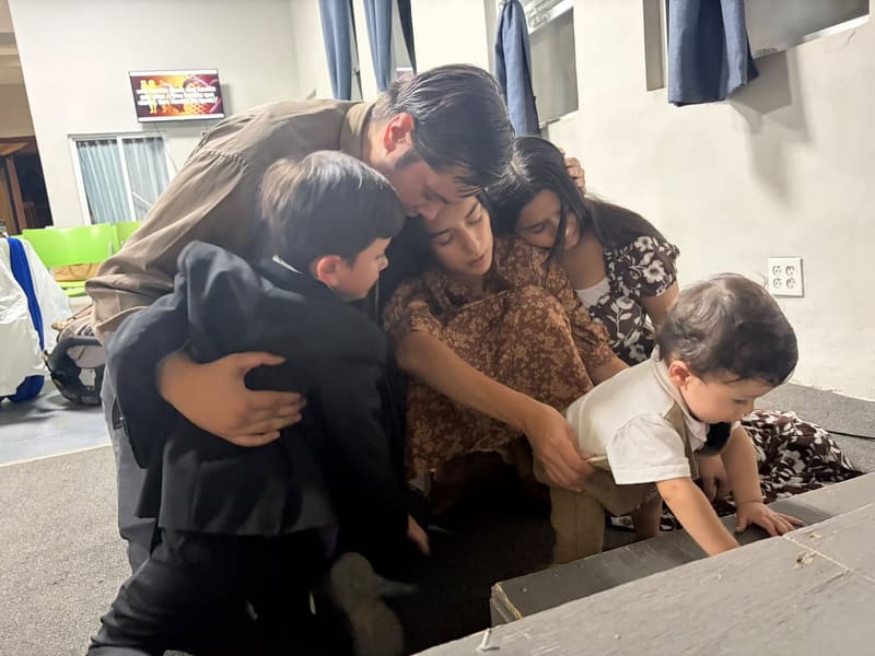 Un hombre, dos mujeres y dos niños pequeños orando abrazados al frente de una iglesia.
