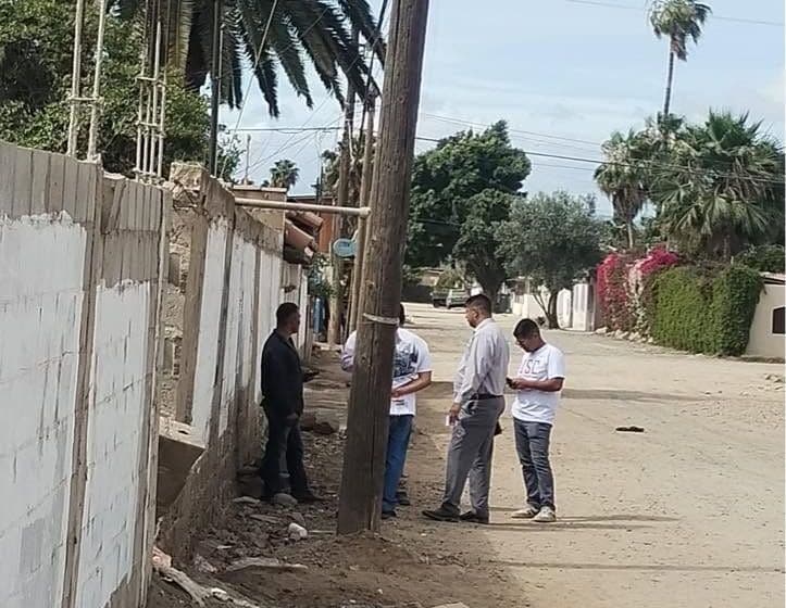 Miembros de la iglesia platican con personas en una calle de terracería de un barrio, junto a una barda.