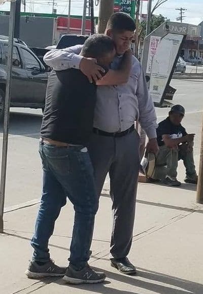 Un miembro de la iglesia abraza a un hombre y ora con él en una banqueta de la ciudad.
